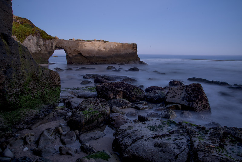 Long exposure blue hour shot of coastal sea arch with silky water washing over rocks